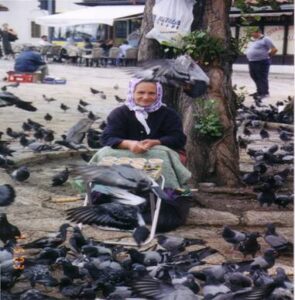 The Duck Masked & Crowned Bird Goddess dressed in her bolero jacket (Late Vinca Culture, 4500 BCE) is mirrored in the Sarajevo Stari Baba making a living from selling seeds so that others can see HER-the Bird Goddess. 